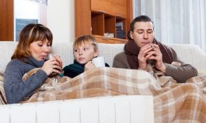 freezing family of three with cups of tea warming near warm radiator in home