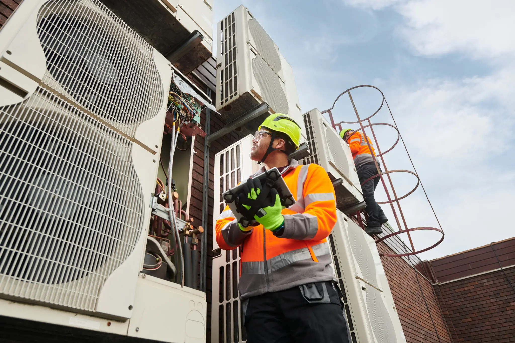 Technician inspecting an HVAC unit outdoors wearing safety gear.