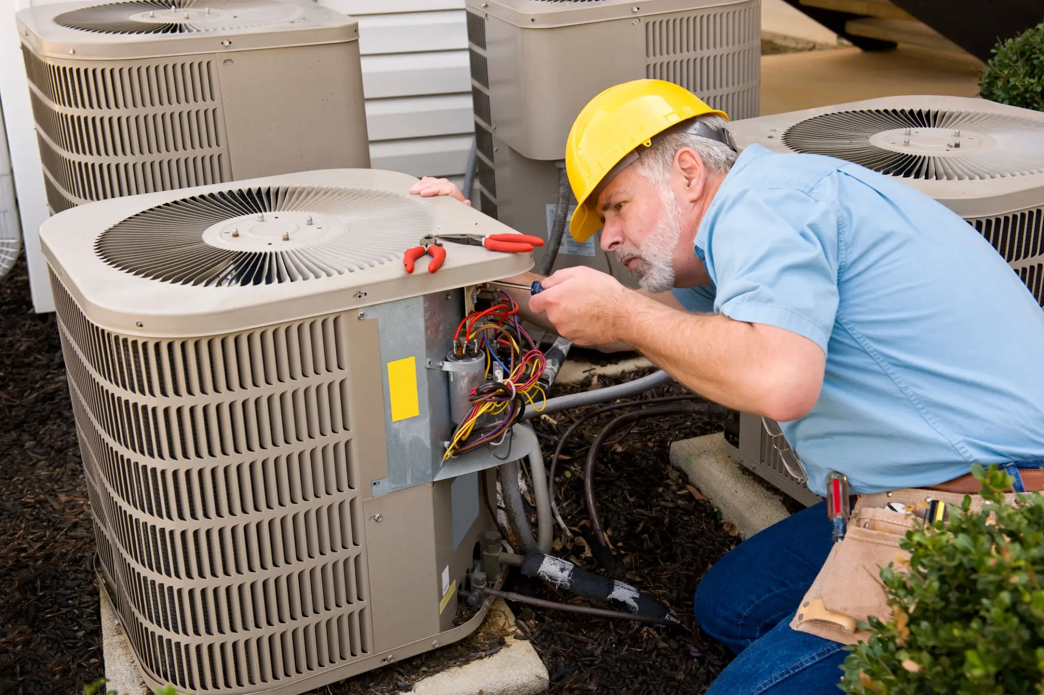 Technician repairing an air conditioning unit outdoors.
