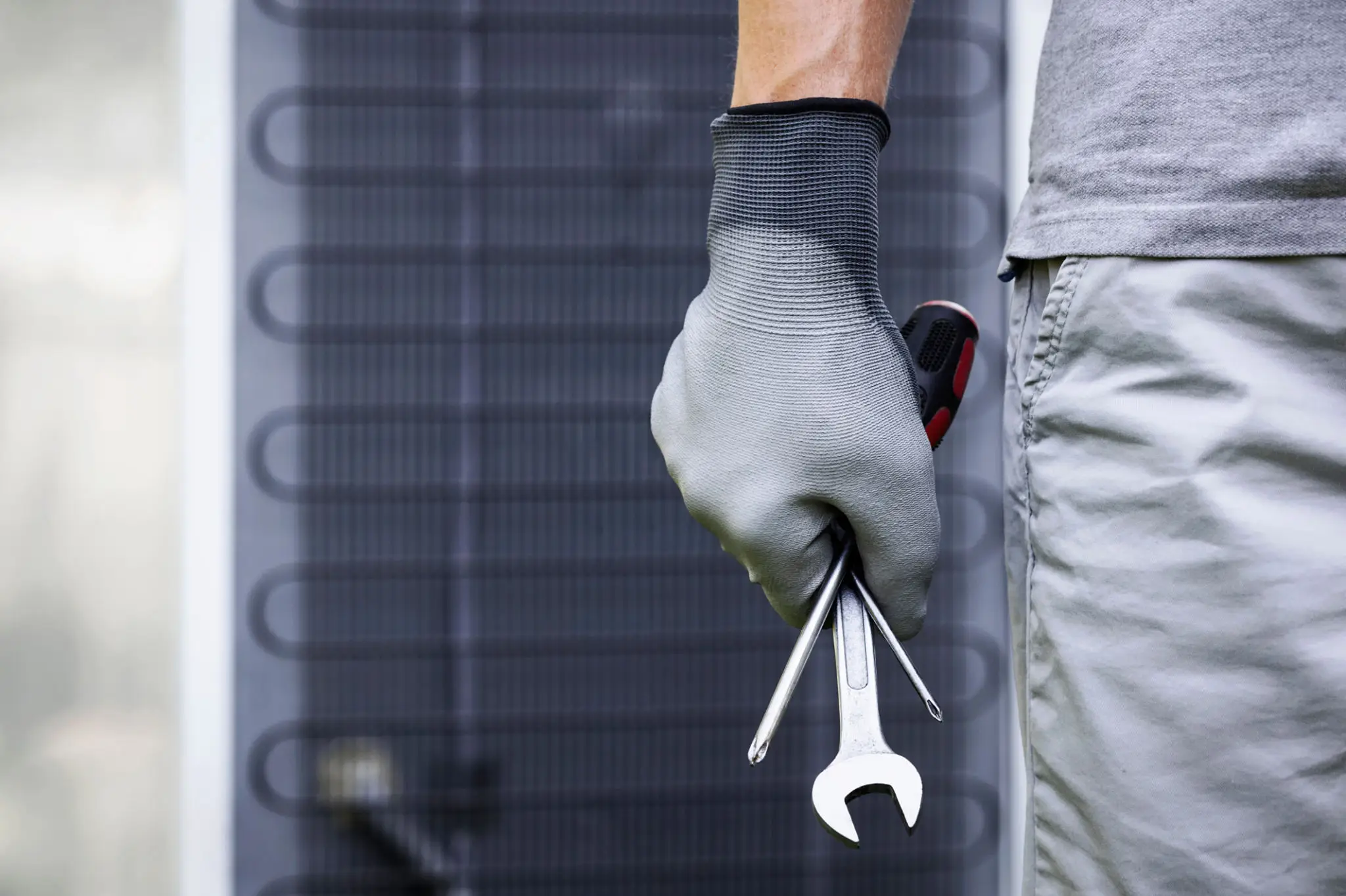 Technician holding a wrench and screwdriver near an HVAC unit.