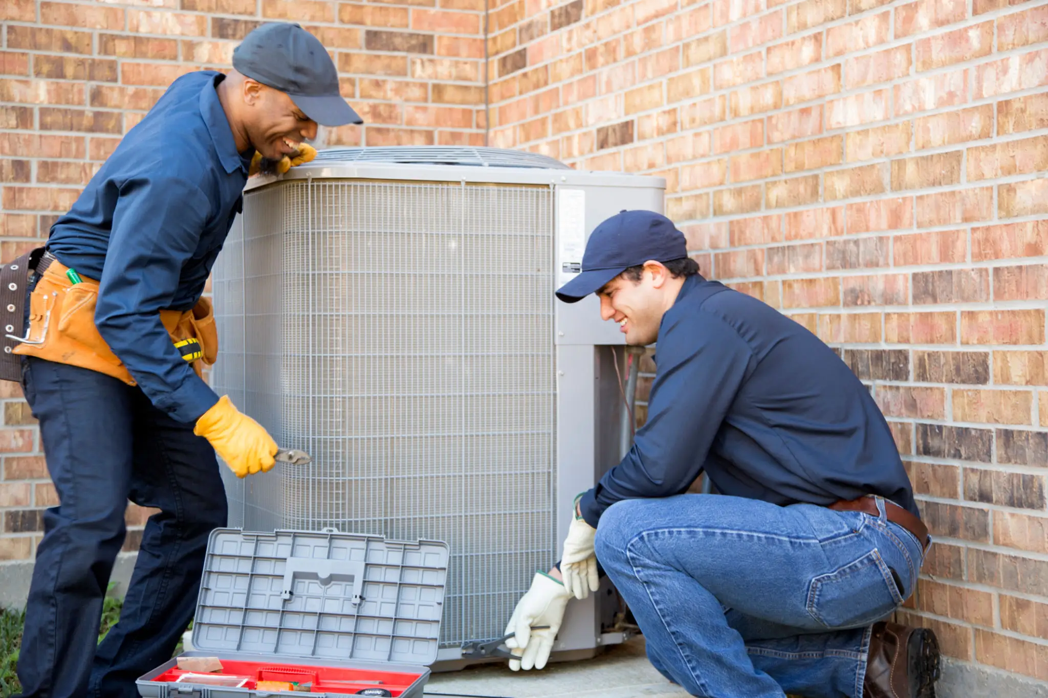 Two technicians repairing an outdoor HVAC unit.